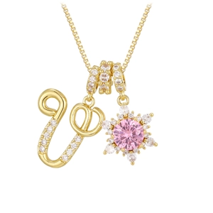 Macro detail of golden snowflake pendant with large pink gemstone and crystal letter U
