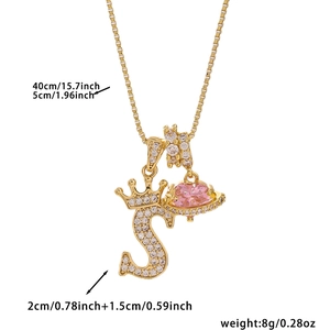 Detail of gold necklace with letter S pendant, crown motif and pink heart charm