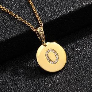 Primer plano del colgante letra O dorado con circonitas sobre una textura negra