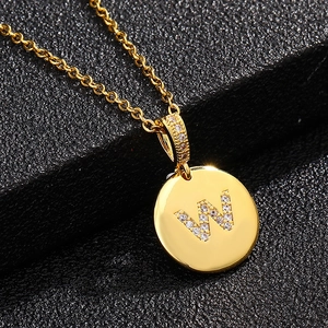 Vista macro de un collar dorado con colgante redondo y letra W de circonitas