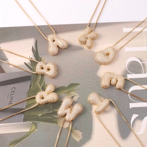 Macro view of eight gold bubble letter necklaces with pavé zircon stones on grey background