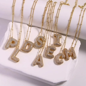 Gold balloon alphabet necklaces with pavé zircon crystals on white display stand