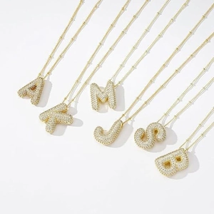 Macro shot of gold bubble initial pendants with pavé zircon settings on satellite chains