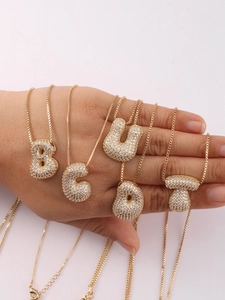 Close-up of gold bubble letter pendants with pave zircon on a box chain held in hand