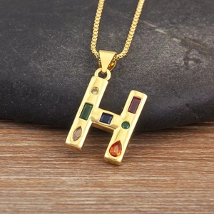Primer plano del colgante letra H dorado con piedras de circonia de colores y fondo natural
