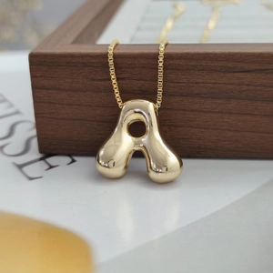 Macro shot of gold bubble initial A pendant on a box chain over a wooden box