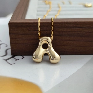 Macro detail of golden balloon style puffy letter A pendant necklace on a jewelry box