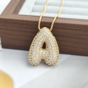 Close-up of golden letter A bubble pendant with micro-pave crystals on wooden stand