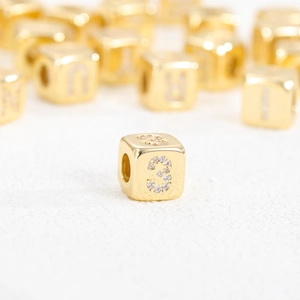 Vista macro di una perla a cubo in oro 18k con numero 3 in zirconi per creazione gioielli fai-da-te