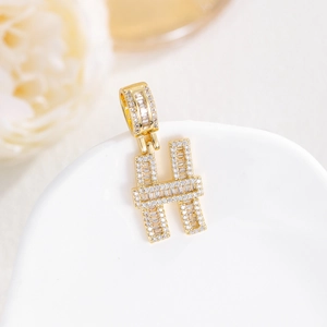 Dettaglio del ciondolo lettera H dorato con micro pavé di zirconi su vassoio bianco