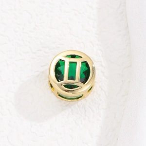 Detalle de un colgante circular hueco dorado con una piedra preciosa verde esmeralda