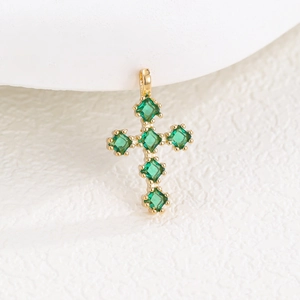 Gros plan du pendentif croix dorée serti de six zircons vert émeraude sur fond blanc