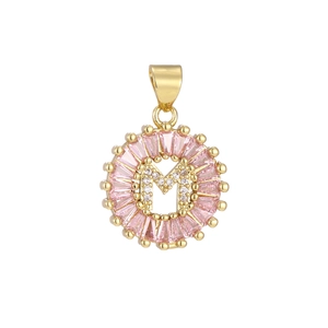 Macro shot of gold pendant with letter M, pink baguette stones and micro zircon pavé