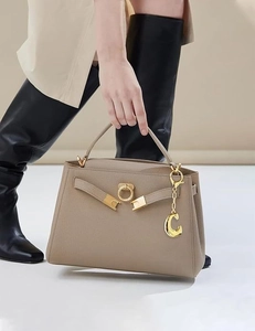 Dettaglio del ciondolo lettera C dorata su borsa in pelle taupe con chiusura dorata