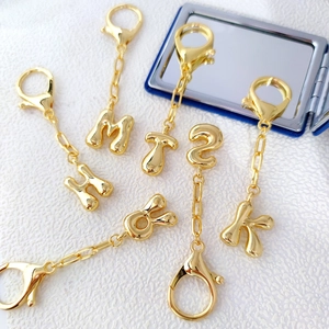 Vista dettagliata dei ciondoli placcati in oro 18K con font a bolla e chiusura a moschettone