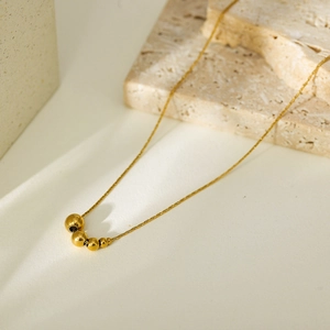 Detail of gold titanium steel necklace with five graduated solid beads on stone