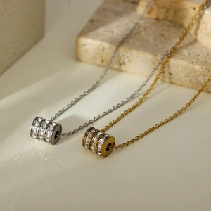 Detail of silver and gold cylinder pendants with three rows of pavé crystals on thin chains