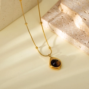 Elegant gold-tone beaded necklace with a cat-eye tiger eye teardrop pendant in warm lighting