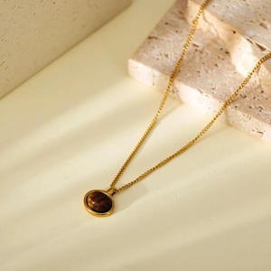 Close-up of a gold necklace with a round tiger eye stone pendant on a stone base