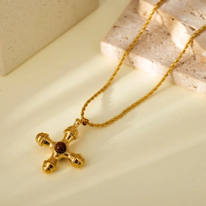 Close-up of a gold cross necklace with rope chain and a central brown bead inlay