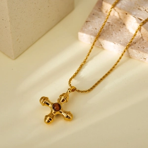 Golden cross necklace with tiger eye stone and twisted rope chain on stone base