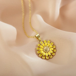 Golden sunflower necklace featuring vibrant yellow enamel petals on soft peach fabric