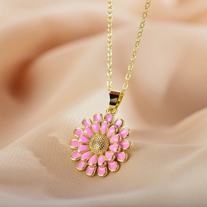 Macro detail of gold necklace with pink enamel sunflower pendant on silk background