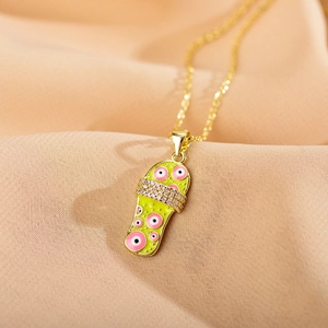 Macro detail of gold necklace with light green enamel slipper pendant and pink evil eye design