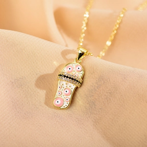 Close-up of golden slipper pendant with white enamel, evil eye pattern and zircon inlay