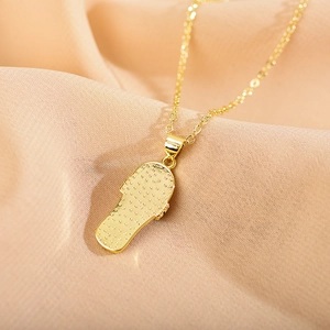 Detailed close-up of a gold-plated slipper pendant necklace on pink fabric background