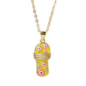 Close-up of golden flip-flop pendant with green enamel, pink evil eyes and rhinestones
