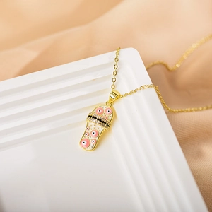 Close-up of gold-plated flip-flop pendant with white enamel and pink evil eye charms