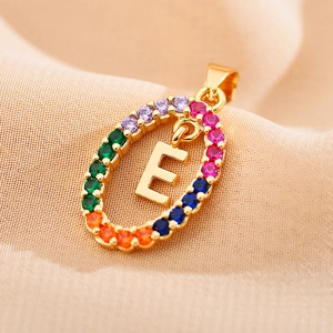 Close-up of golden oval letter E pendant with multi-color zircon stones on beige fabric