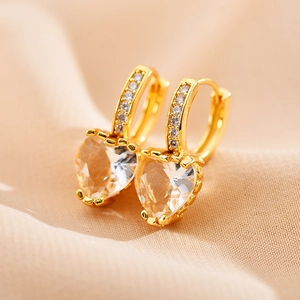 Détail macro de boucles d'oreilles cœur dorées avec zircons sur un fond en soie élégant