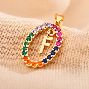 Macro detail of gold oval pendant with rainbow zircons and a central letter F