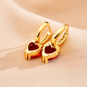 Détail macro de boucles d'oreilles créoles dorées avec zircons rouges en forme de cœur