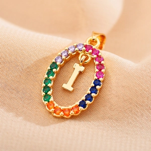 Macro shot of gold oval pendant with rainbow zircon stones and letter I detail