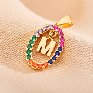 Detailed view of golden oval pendant with letter M and colorful zircon stones
