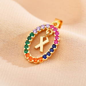 Detailed macro of gold oval pendant with colorful zircons and central letter X design