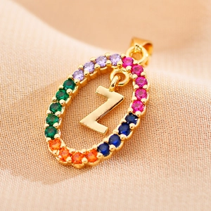 Macro detail of gold letter Z pendant with colorful zircon stones on beige fabric