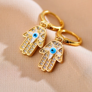 Macro-opname van gouden Hamsa-hand oorbellen met Evil Eye en kristallen op beige stof