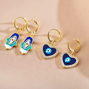 Detailopname van Evil Eye en Hamsa oorbellen op satijn, goud met blauw email en zirkonia