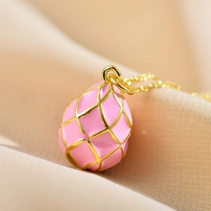 Macro view of a pink enamel egg pendant with gold lattice patterns on silk fabric