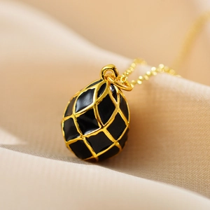 Macro detail of egg-shaped black enamel pendant with golden grid on silk background