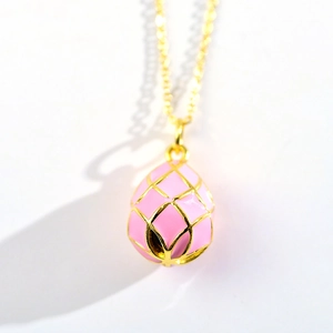 Close-up of golden necklace featuring a delicate pink enamel egg-shaped planet pendant