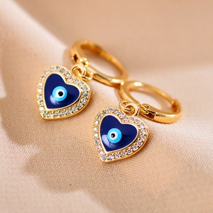 Macro-opname van gouden oorringen met blauwe emaille harten en boze oog details