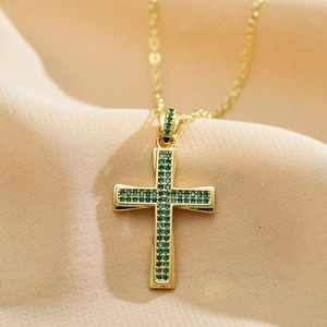 Detailed close-up of a gold-plated cross pendant featuring emerald green zircon stones