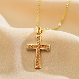Macro view of gold cross pendant with micro-pave orange stones on pleated fabric