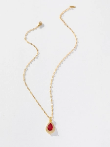 Detailed view of a gold teardrop pendant with red gemstone and halo of white diamonds