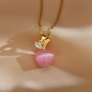 Vue macro du pendentif pomme en œil de chat rose avec chaîne dorée sur du tissu